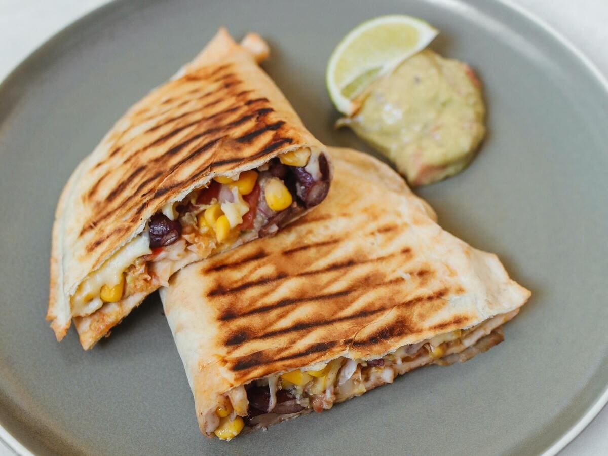 Two vegetarian quesadillas with corn and lime on a plate.