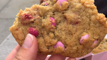 A person holding up a pink and white crumbl cookie.